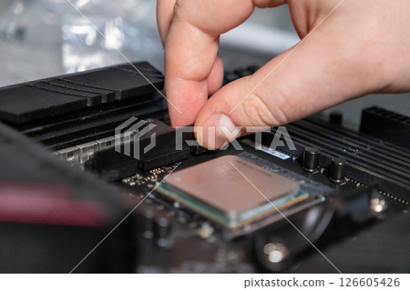nserting component onto computer motherboard, close-up of hand fixing hardware during pc assembly 126605426