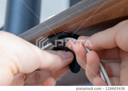 hands fastening cable with velcro strap under wooden desk, improving cable management in workspace hands fastening cable with velcro strap under wooden desk, improving cable management in workspace 126605436