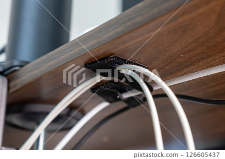 cable management under wooden desk using black velcro straps, showcasing organized wiring setup for efficient workspace arrangement, close-up view 126605437