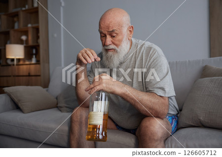 Sad senior man drinking alcohol alone sitting on the couch at home 126605712