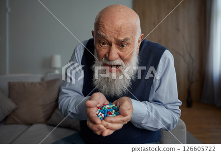 Frustrated senior man holding lots of pills in palms facing forward to camera Frustrated senior man holding lots of pills in palms facing forward to camera 126605722