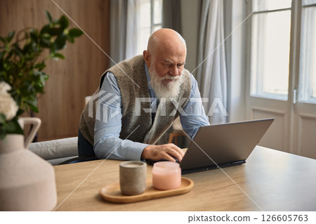 Senior man using laptop computer sitting at home 126605763