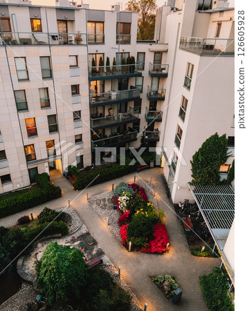 High angle view of courtyard with playground, garden, and illuminated paved walkways, surrounded by modern residential buildings with balconies, at dusk. Modern residential towers with balconies 126605928