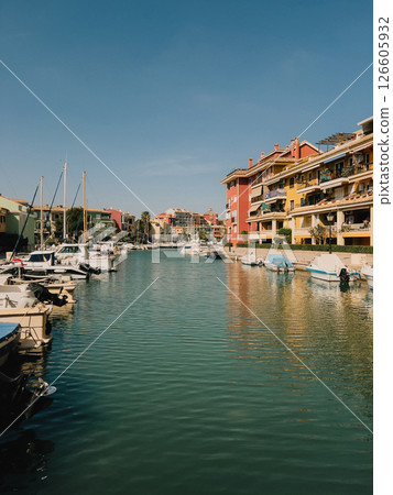 Colorful buildings reflecting on calm marina waters, filled with boats, create picturesque scene under sunny sky, embodying coastal leisure and vibrant architecture. Waterfront, marina, sailboat, boat 126605932