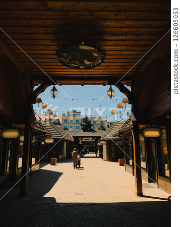 Tourist walking away from camera under charming wooden passage in heart of Zakopane, Poland, enjoying sunny summer day filled with exploration and discovery. Wooden archway, warm sunlight 126605953