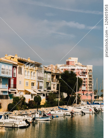 Colorful buildings stand along marina with moored boats under cloudy sky, creating vibrant and picturesque scene in Spanish coastal town. Colorful marina buildings lining waterfront with moored boats 126605958