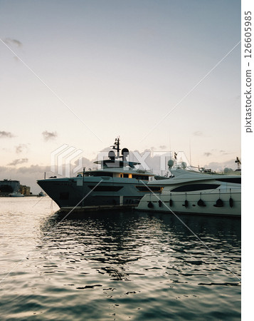 Two large yachts are moored in harbor at sunset, their sleek silhouettes reflected in calm water, creating scene of luxury and tranquility. Luxury yachts moored during golden sunset, maritime ambiance Two large yachts are moored in harbor at sunset, their sleek silhouettes reflected in calm water, creating scene of luxury and tranquility. Luxury yachts moored during golden sunset, maritime ambiance 126605985