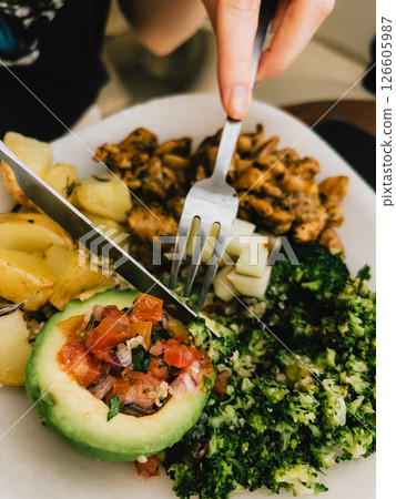 First-person view: Hands skillfully using cutlery while enjoying a healthy, balanced meal featuring broccoli, avocado, potatoes, and quinoa, highlighting fresh and nutritious ingredients. First-person view: Hands skillfully using cutlery while enjoying a healthy, balanced meal featuring broccoli, avocado, potatoes, and quinoa, highlighting fresh and nutritious ingredients. 126605987