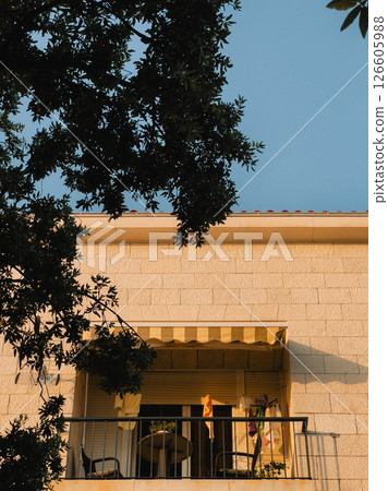 Clothes drying on balcony during golden hour, with tree branches framing scene and yellow and white awning casting gentle shade, creating warm, cozy atmosphere. Sunlight, laundry, urban balcony Clothes drying on balcony during golden hour, with tree branches framing scene and yellow and white awning casting gentle shade, creating warm, cozy atmosphere. Sunlight, laundry, urban balcony 126605988