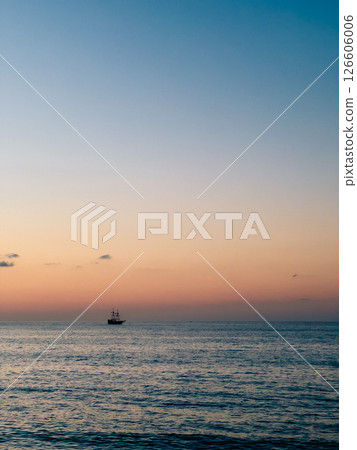 Wooden galleon sailing across tranquil ocean waters, golden sunset casting warm orange and pink light, evoking maritime history and serene nautical atmosphere. Galleon sails away on calm sea, sun sets 126606006