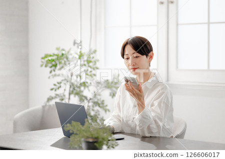 A woman operating a computer while holding a smartphone A woman operating a computer while holding a smartphone 126606017