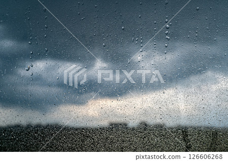Rain shower on car windshield or car window and blurry road in background. Driving in rainy season. Rain drops on car mirror. Storm clouds, tornado, safety. 126606268