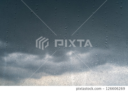 Rain shower on car windshield or car window and blurry road in background. Driving in rainy season. Rain drops on car mirror. Storm clouds, tornado, safety. 126606269