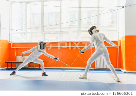Female fencer making epee hit on opponent sneaker indoors. 126606361