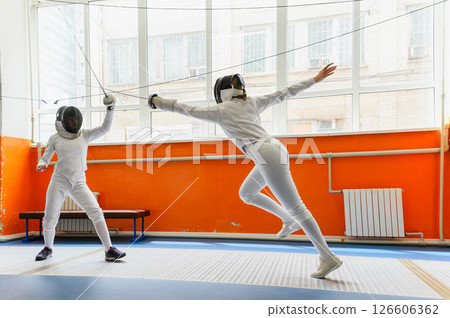 Female fencer making airborne epee attack in bright fencing hall. Female fencer making airborne epee attack in bright fencing hall. 126606362