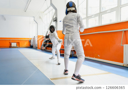 Female fencer lunging toward opponent in bright fencing hall. Female fencer lunging toward opponent in bright fencing hall. 126606365
