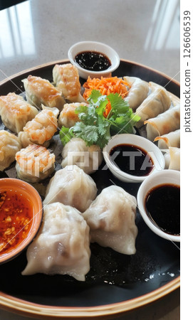 A variety of dim sum dishes are arranged beautifully on a black platter, showcasing steamed dumplings, shrimp, and flavorful dipping sauces in a lively dining atmosphere 126606539
