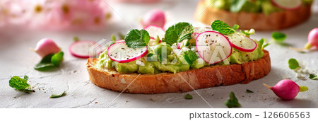 Enjoying a vibrant spring breakfast with creamy avocado spread on toasted bread, garnished with thinly sliced radishes and fresh mint leaves for added flavor, banner Enjoying a vibrant spring breakfast with creamy avocado spread on toasted bread, garnished with thinly sliced radishes and fresh mint leaves for added flavor, banner 126606563
