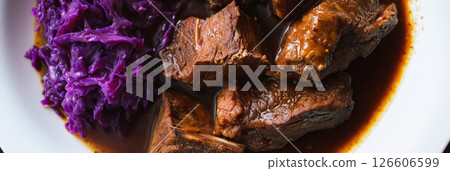 Sauerbraten, a traditional German dish, is presented alongside vibrant purple cabbage, highlighting a hearty meal enjoyed during a family gathering, banner 126606599