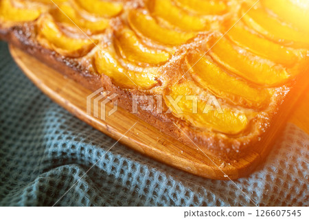 A dessert made of sliced peaches is on a wooden cutting board. The dessert is covered in sugar and looks delicious. A dessert made of sliced peaches is on a wooden cutting board. The dessert is covered in sugar and looks delicious. 126607545