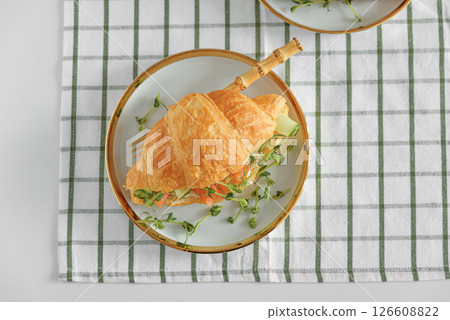 Croissant sandwich with salmon, onions and microgreens on white table. Healthy breakfast. Top view Croissant sandwich with salmon, onions and microgreens on white table. Healthy breakfast. Top view 126608822
