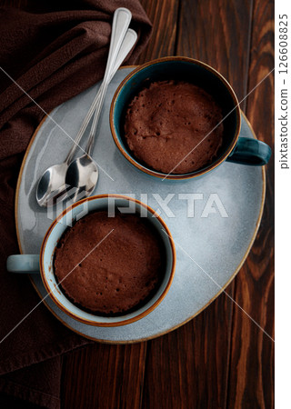Two chocolate mug cakes on dark wooden table. Easy homemade dessert. Mugcake from microwave. Top view Two chocolate mug cakes on dark wooden table. Easy homemade dessert. Mugcake from microwave. Top view 126608825