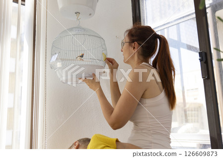 Woman feeding small bird in hanging cage at home 126609873