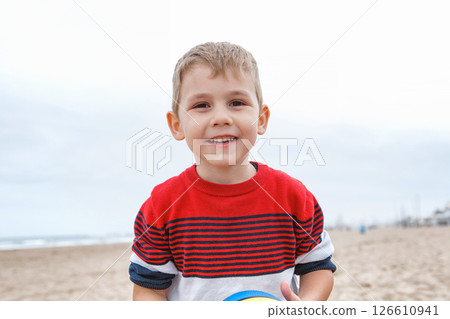 Young Boy Playing With a Colorful Beach Ball on a Sandy Shoreline During a Cloudy Afternoon 126610941