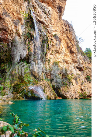 A Cascading Waterfall Flows Down a Rocky Cliff Surrounded by Lush Greenery Near a Natural Landscape 126610950