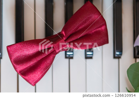Red Satin Bow Tie Resting on Black and White Piano Keys in a Stylish Setting. Red Satin Bow Tie Resting on Black and White Piano Keys in a Stylish Setting. 126610954