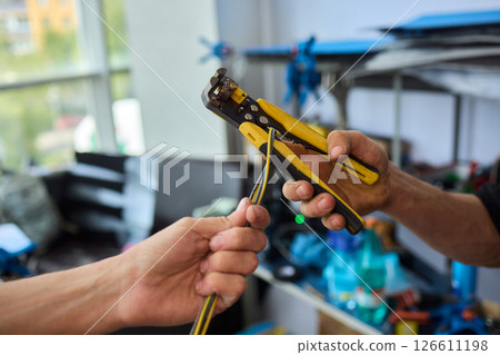 Two hands actively exchanging wire strippers in a well-organized workshop environment 126611198