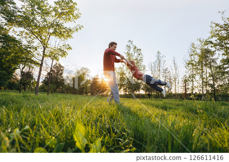 Father spinning son in park at sunset Father spinning son in park at sunset 126611416