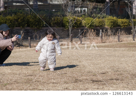[一名一歲大的兒童和他的母親在相模原市立麻溝公園的草地上玩耍，玩著智慧型手機] 126613143