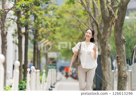 一名女子拿著智慧型手機在城裡走來走去 一名女子拿著智慧型手機在城裡走來走去 126613296