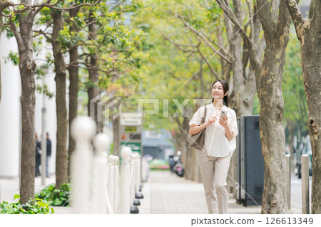 一名女子拿著智慧型手機在城裡走來走去 一名女子拿著智慧型手機在城裡走來走去 126613349