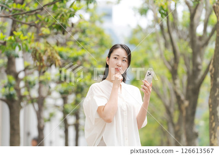 一名女子拿著智慧型手機在城裡走來走去 126613567
