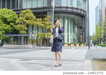 一位年輕的女商人手裡拿著智慧型手機站在辦公區 126613731