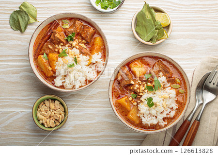 Two bowls of delicious massaman curry with beef, potatoes, rice, and peanuts, garnished with parsley on white wooden background, Thai cuisine 126613828
