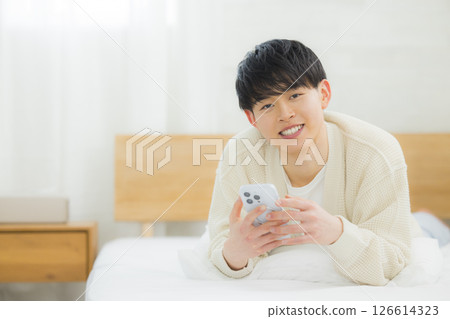 年輕人在床上使用智慧型手機 年輕人在床上使用智慧型手機 126614323