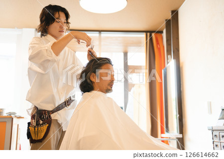 A male stylist cutting a haircut and an elderly male customer A male stylist cutting a haircut and an elderly male customer 126614662