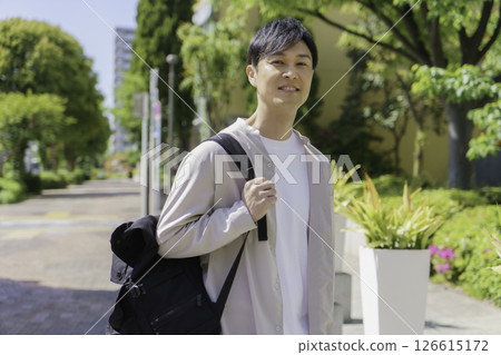 A middle-aged man walking through a city with fresh greenery 126615172