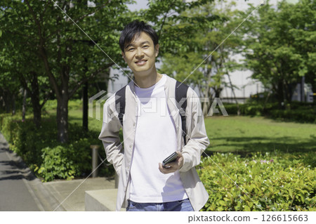 一位中年男子手裡拿著智慧型手機，走在綠色城市中 126615663