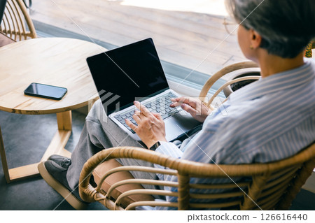 Senior woman working on laptop in cozy chair by window, wearing striped shirt, top view 126616440