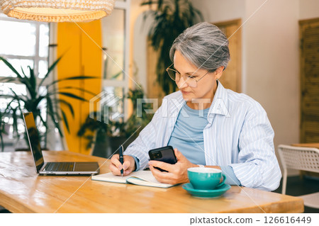 Mature Woman Freelancing from Cafe with Laptop, Coffee and Smartphone Work and Balance Lifestyle 126616449