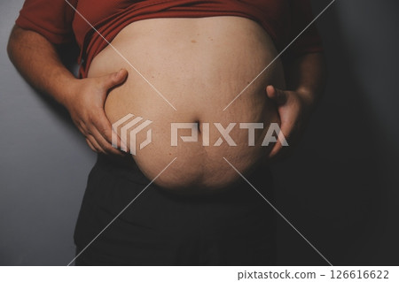 Asian fat man in front of a mirror looks at his body. Excess belly fat, Unhealthy lifestyle, Diet concept. 126616622