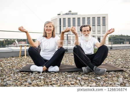 Senior man and woman performing yoga meditation in lotus pose on urban rooftop. Relaxation mindfulness wellness and bonding activities for older adults embracing active and healthy lifestyles outdoors Senior man and woman performing yoga meditation in lotus pose on urban rooftop. Relaxation mindfulness wellness and bonding activities for older adults embracing active and healthy lifestyles outdoors 126616874