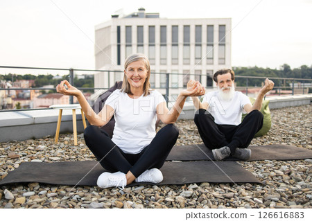 Senior man and woman practicing yoga in lotus pose on rooftop terrace outdoors. 126616883
