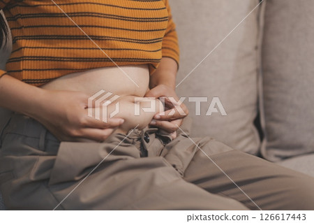 Cropped shot of woman touching and squeezing her fat belly. Cropped shot of woman touching and squeezing her fat belly. 126617443
