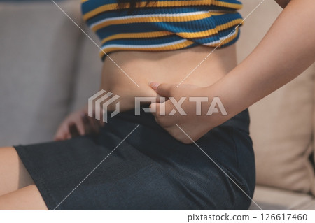 Cropped shot of woman touching and squeezing her fat belly. 126617460