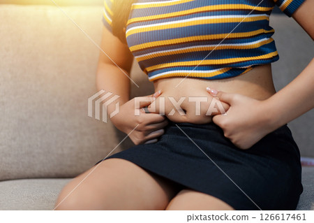 Cropped shot of woman touching and squeezing her fat belly. Cropped shot of woman touching and squeezing her fat belly. 126617461